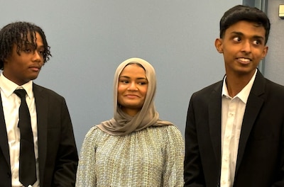 Two young men in dark jackets stand next to a woman in a hijab.