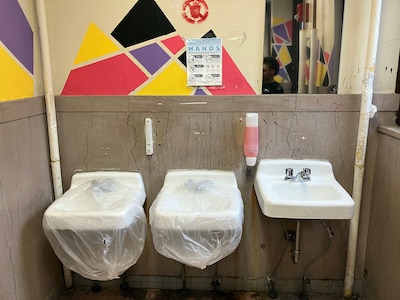 Three handwashing sinks in a high school bathroom, two of them are wrapped in plastic.