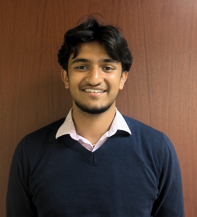 Headshot of a teen wearing a white collared shirt and a navy blue sweater.